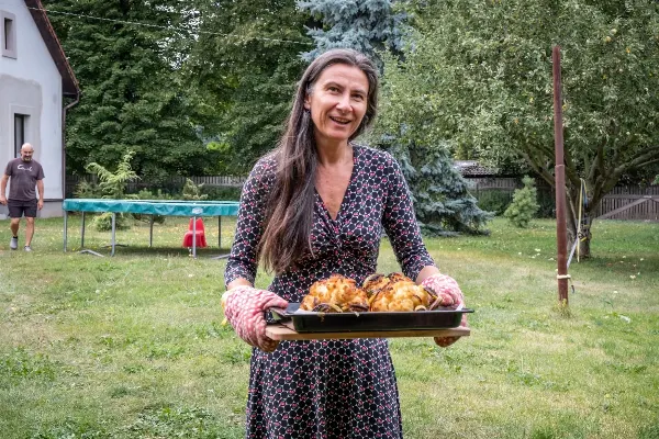 Žena s pekáčem masem na zahradě nese jídlo pro účastníky.