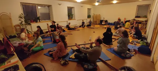 Skupinový workshop s didgeridoo - účastníci sedí na yoga-matkách a hrají na didgeridoo.