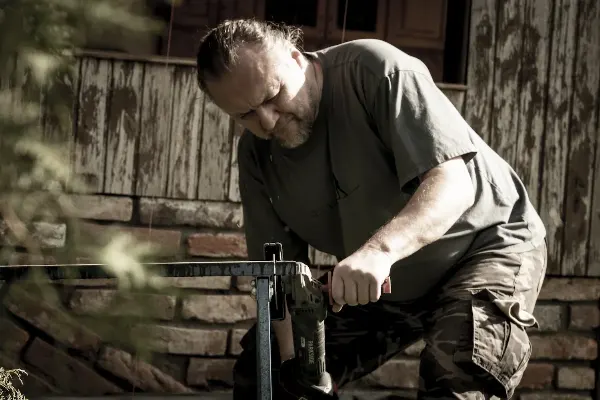 Dan pracuje s elektrickým nástrojem na zahradě u dřevěné konstrukce.